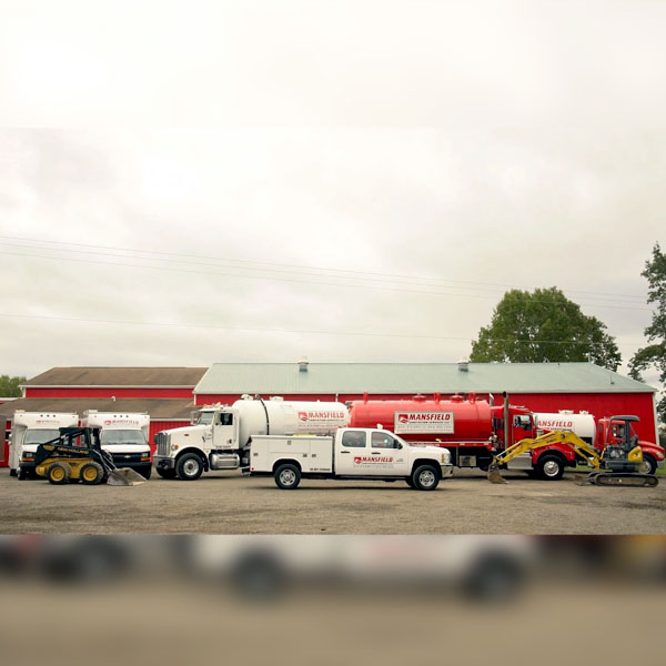 Mansfield Sanitation trucks parked in front of a red barn. Proudly serving Erie, Meadville, Crawford County, PA, and the surrounding areas.
