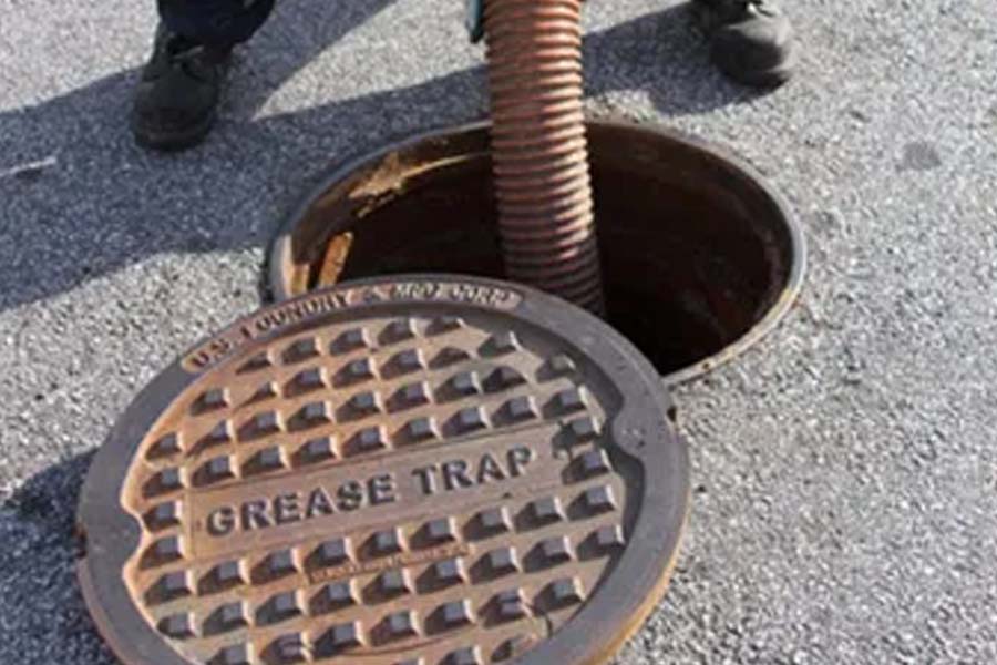 A hose going into an open grease trap to clean the drain.