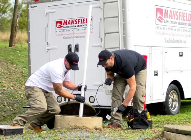 Two Mansfield Sanitation Services employees inspecting and pumping sewage from a septic tank.