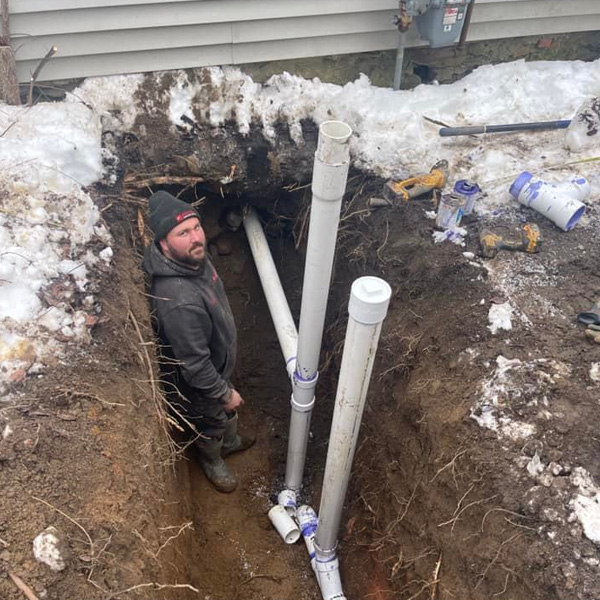 A Mansfield service technician standing in an excavated trench installing new plumbing pipes.
